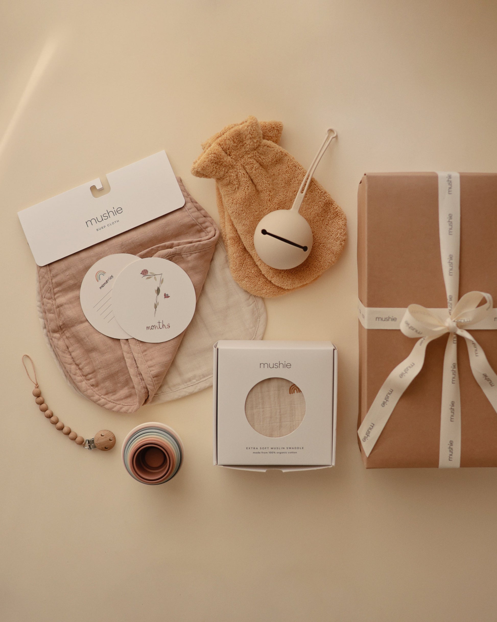 Collection of baby products including a gift box, pacifier, and other items on a beige background.