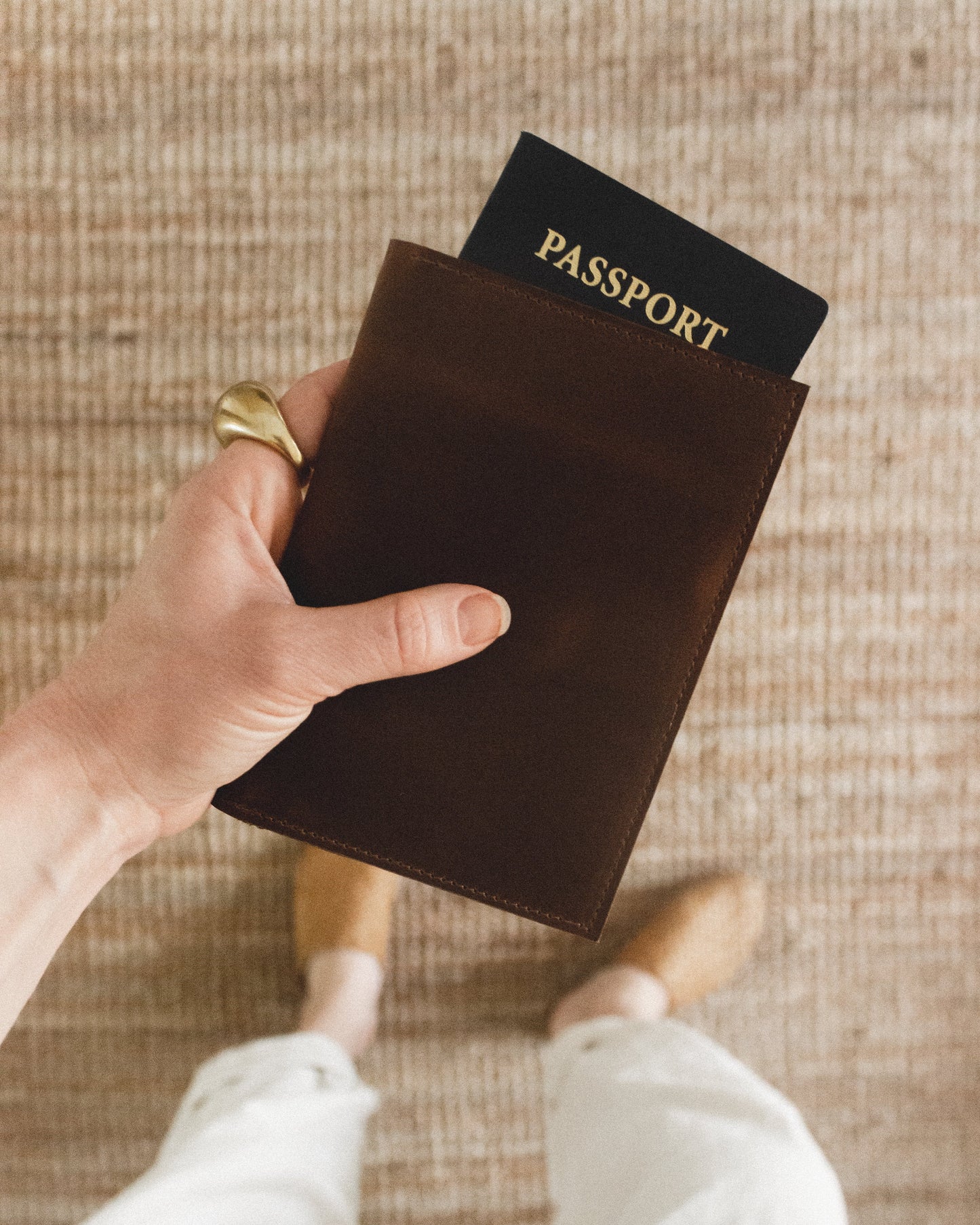 Hand holding a brown passport holder with a passport on a textured surface