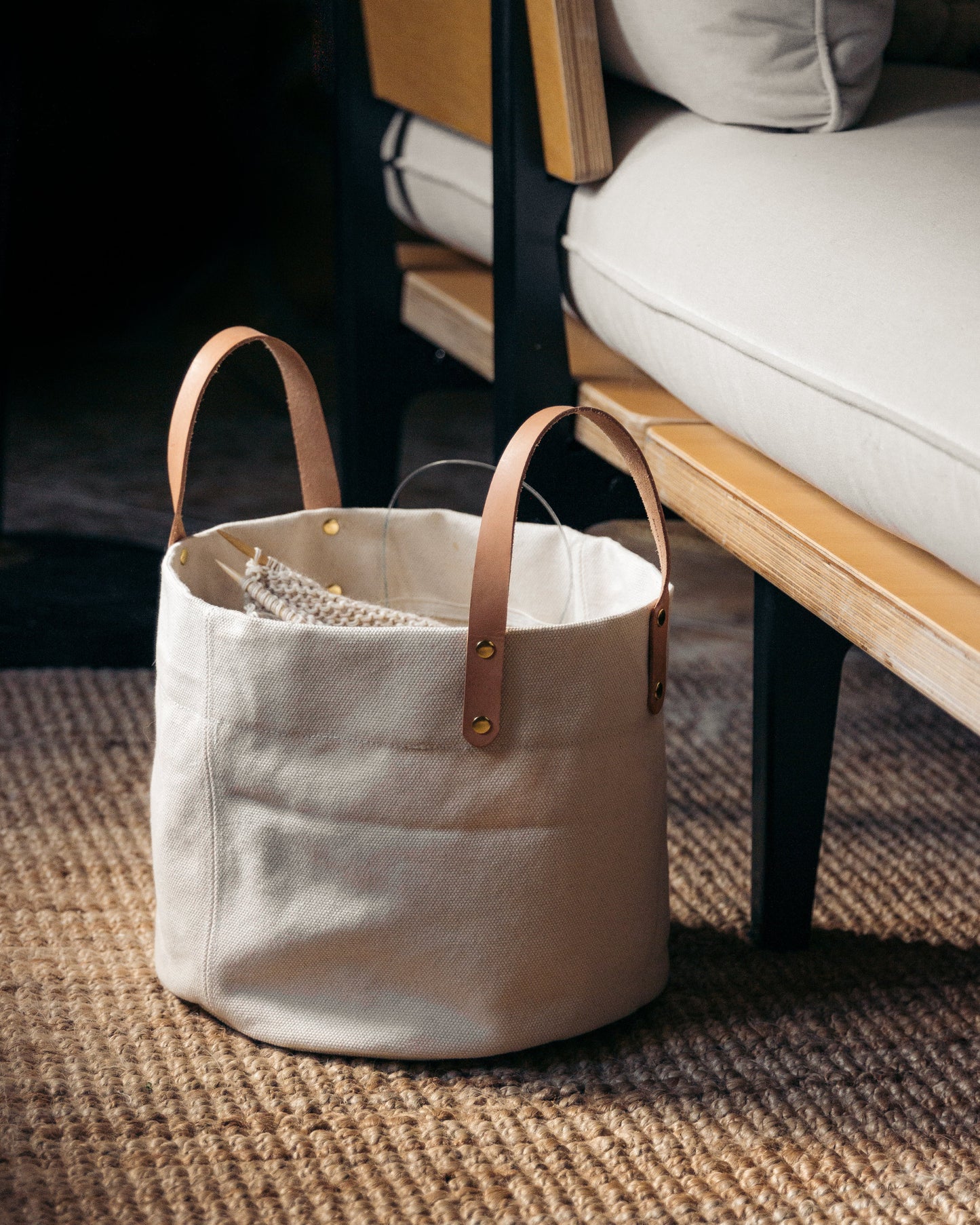 White canvas bag with leather handles on a textured surface next to a sofa.