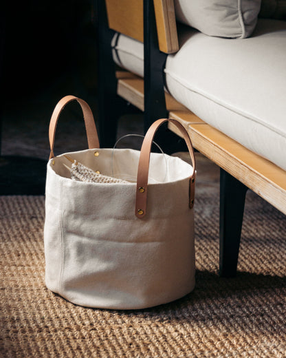 White canvas bag with leather handles on a textured surface next to a sofa.
