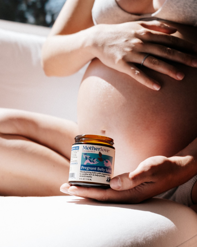 Pregnant woman holding a jar of Motherlove product against her belly.