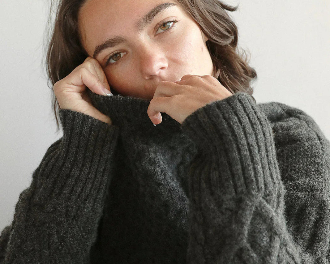 Woman wearing a dark gray cable knit sweater against a plain background